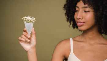 A woman holds a menstrual cup with white flowers coming out of it.