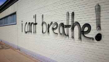 A white brick wall is spray painted, "I can't breathe!"